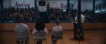 Movie still from “The Binge” (2020), directed by Jeremy Garelick – Two people sitting in chairs in front of a crowd; Wide shot, Over the shoulder angle