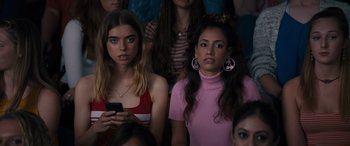 Movie still from “The Binge” (2020), directed by Jeremy Garelick – Two young women sitting next to each other in front of a group of people; Close Up shot, High angle