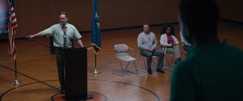 Movie still from “The Binge” (2020), directed by Jeremy Garelick – A man standing in front of a podium and two women sitting in chairs; Wide shot, Over the shoulder angle