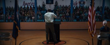 Movie still from “The Binge” (2020), directed by Jeremy Garelick – A man standing in front of a podium in front of a crowd of people; Wide shot, High angle