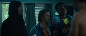 Movie still from “The Binge” (2020), directed by Jeremy Garelick – A man standing next to another man in front of a window; Medium shot, Low angle