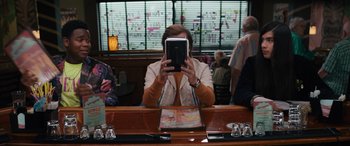 Movie still from “The Binge” (2020), directed by Jeremy Garelick – A person sitting at a table holding a tablet; Medium shot, Over the shoulder angle