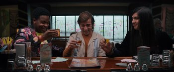 Movie still from “The Binge” (2020), directed by Jeremy Garelick – A man sitting at a table with a glass of whiskey; Medium shot, Low angle