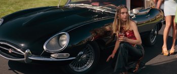 Movie still from “The Binge” (2020), directed by Jeremy Garelick – A woman standing in front of a black car; Medium shot, High angle