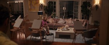 Movie still from “The Binge” (2020), directed by Jeremy Garelick – A woman sitting on a chair in front of a coffee table; Wide shot, High angle