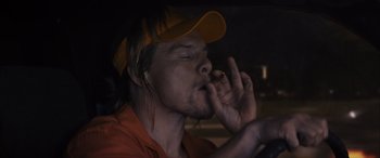 Movie still from “The Binge” (2020), directed by Jeremy Garelick – A man in a baseball cap is smoking a cigarette; Medium shot, Overhead angle