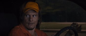 Movie still from “The Binge” (2020), directed by Jeremy Garelick – A man in an orange shirt and a yellow hat holding a gun; Close Up shot, Over the shoulder angle