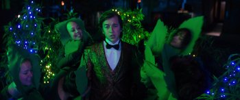 Movie still from “The Binge” (2020), directed by Jeremy Garelick – A man in a suit and bow tie standing next to a woman in a green dress; Medium shot, Over the shoulder angle