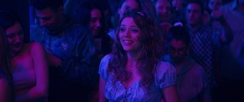 Movie still from “The Binge” (2020), directed by Jeremy Garelick – A woman smiles brightly at a concert in the dark; Medium shot, Over the shoulder angle