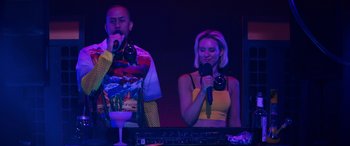 Movie still from “The Binge” (2020), directed by Jeremy Garelick – A man and a woman singing into microphones; Medium shot, Low angle