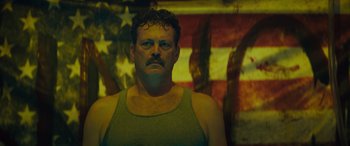 Movie still from “The Binge” (2020), directed by Jeremy Garelick – A person wearing a tank top with an american flag in the background; Close Up shot, Low angle