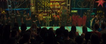 Movie still from “The Binge” (2020), directed by Jeremy Garelick – A group of people standing in front of an american flag; Wide shot, Low angle