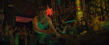 Movie still from “The Binge” (2020), directed by Jeremy Garelick – A man in a green tank top is playing a game with a dog; Medium shot, Low angle