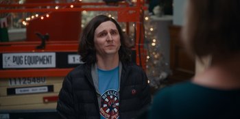 Movie still from “It's A Wonderful Binge” (2022), directed by Jordan VanDina – A man with long black hair wearing a black jacket; Medium shot, Over the shoulder angle