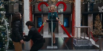 Movie still from “It's A Wonderful Binge” (2022), directed by Jordan VanDina – A woman standing in front of a microphone; Medium shot, Low angle