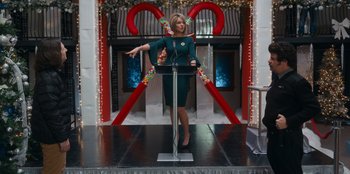 Movie still from “It's A Wonderful Binge” (2022), directed by Jordan VanDina – A woman standing on a stage in front of a microphone; Medium shot, Low angle