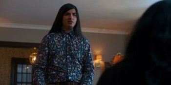 Movie still from “It's A Wonderful Binge” (2022), directed by Jordan VanDina – A man with long black hair wearing a floral shirt; Medium shot, Over the shoulder angle