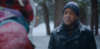 Movie still from “It's A Wonderful Binge” (2022), directed by Jordan VanDina – A man standing in the snow looking at the camera; Close Up shot, Over the shoulder angle