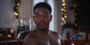 Movie still from “It's A Wonderful Binge” (2022), directed by Jordan VanDina – A man with a beard is sitting in front of a christmas tree; Close Up shot, Over the shoulder angle