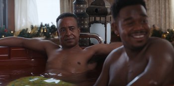 Movie still from “It's A Wonderful Binge” (2022), directed by Jordan VanDina – A man sitting in a tub with another man standing next to him; Medium shot, Over the shoulder angle