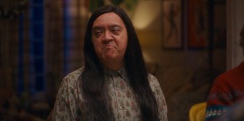 Movie still from “It's A Wonderful Binge” (2022), directed by Jordan VanDina – A man with long black hair wearing a long shirt; Medium shot, Over the shoulder angle