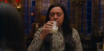 Movie still from “It's A Wonderful Binge” (2022), directed by Jordan VanDina – A person with long hair and a shirt on drinking a glass of milk; Close Up shot, High angle