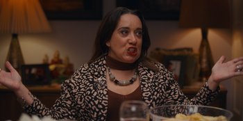 Movie still from “It's A Wonderful Binge” (2022), directed by Jordan VanDina – A woman in a leopard print jacket is making a funny face; Medium shot, Over the shoulder angle