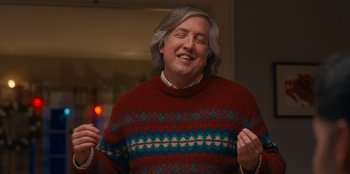 Movie still from “It's A Wonderful Binge” (2022), directed by Jordan VanDina – An older man wearing a red and blue sweater; Medium shot, Low angle