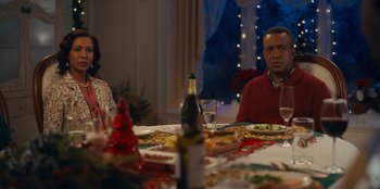 Movie still from “It's A Wonderful Binge” (2022), directed by Jordan VanDina – A man and a woman sitting at a dinner table; Medium shot, Over the shoulder angle