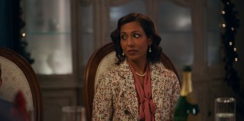 Movie still from “It's A Wonderful Binge” (2022), directed by Jordan VanDina – A woman sitting in a chair wearing a suit; Close Up shot, Over the shoulder angle