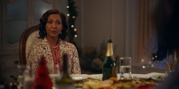 Movie still from “It's A Wonderful Binge” (2022), directed by Jordan VanDina – A woman sitting at a table with a bottle of wine; Medium shot, Over the shoulder angle