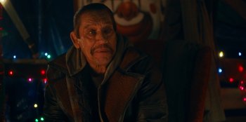 Movie still from “It's A Wonderful Binge” (2022), directed by Jordan VanDina – An older man sitting in front of a painting; Close Up shot, Over the shoulder angle