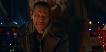 Movie still from “It's A Wonderful Binge” (2022), directed by Jordan VanDina – An older man sitting down with his eyes closed; Medium shot, Over the shoulder angle