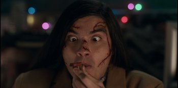 Movie still from “It's A Wonderful Binge” (2022), directed by Jordan VanDina – A woman with a knife in her mouth and blood on her face; Close Up shot, Low angle
