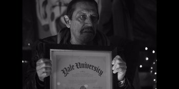Movie still from “It's A Wonderful Binge” (2022), directed by Jordan VanDina – A man holding up a yale university diploma; Close Up shot, Over the shoulder angle