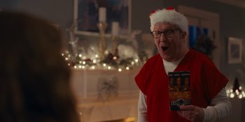 Movie still from “It's A Wonderful Binge” (2022), directed by Jordan VanDina – An older man wearing a santa hat and holding a dvd; Close Up shot, Over the shoulder angle