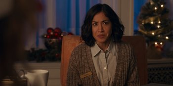 Movie still from “It's A Wonderful Binge” (2022), directed by Jordan VanDina – A woman sitting in a chair in front of a christmas tree; Close Up shot, Over the shoulder angle