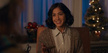 Movie still from “It's A Wonderful Binge” (2022), directed by Jordan VanDina – A woman sitting in a chair holding a piece of paper; Close Up shot, Over the shoulder angle