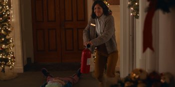 Movie still from “It's A Wonderful Binge” (2022), directed by Jordan VanDina – A woman holding a fire extinguisher in her hand; Medium shot, High angle
