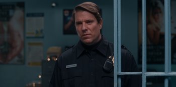 Movie still from “It's A Wonderful Binge” (2022), directed by Jordan VanDina – A man in a police uniform standing in front of a window; Close Up shot, Low angle