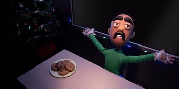Movie still from “It's A Wonderful Binge” (2022), directed by Jordan VanDina – A toy man sitting in front of a plate of chocolate chip cookies; Medium shot, Over the shoulder angle