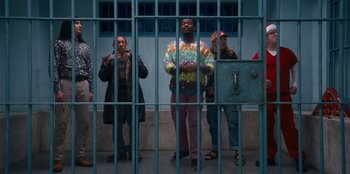 Movie still from “It's A Wonderful Binge” (2022), directed by Jordan VanDina – A group of people standing in front of a metal fence; Wide shot, Low angle