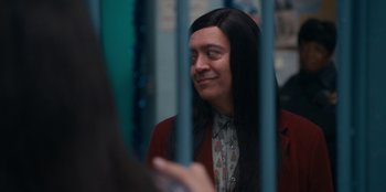 Movie still from “It's A Wonderful Binge” (2022), directed by Jordan VanDina – A man with long hair and a shirt is looking through a fence; Close Up shot, Over the shoulder angle