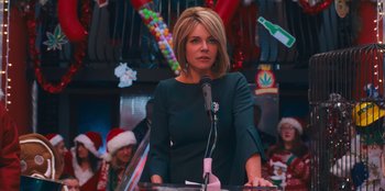 Movie still from “It's A Wonderful Binge” (2022), directed by Jordan VanDina – A woman standing at a podium in front of a microphone; Close Up shot, Over the shoulder angle