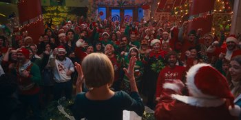 Movie still from “It's A Wonderful Binge” (2022), directed by Jordan VanDina – A group of people wearing santa hats and holding hands; Extreme Wide shot, High angle