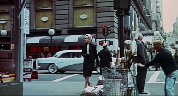 Movie still from “The Birds” (1963), directed by Alfred Hitchcock – A woman is crossing the street on a busy street; Wide shot, Low angle