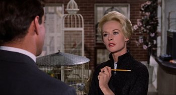 Movie still from “The Birds” (1963), directed by Alfred Hitchcock – A woman holding a pencil in her hand while standing in front of a cage; Close Up shot, Over the shoulder angle