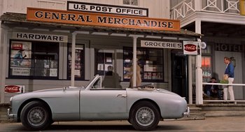 Movie still from “The Birds” (1963), directed by Alfred Hitchcock – An old car parked in front of a post office; Wide shot, High angle