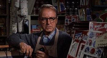 Movie still from “The Birds” (1963), directed by Alfred Hitchcock – An older man wearing glasses and a brown apron; Close Up shot, Low angle