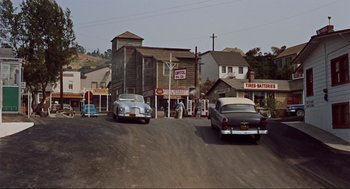 Movie still from “The Birds” (1963), directed by Alfred Hitchcock – An old time gas station with cars parked on the side of the road; Extreme Wide shot, High angle